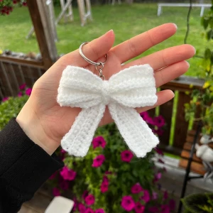 Vit virkad rosett nyckelring - Superfin handgjord vit rosett i virkat material som nyckelring. Perfekt att hänga på väskan eller nycklarna för en söt och personlig touch. Rosetten är fluffig och har en klassisk form med två långa band. Gjord av mig!