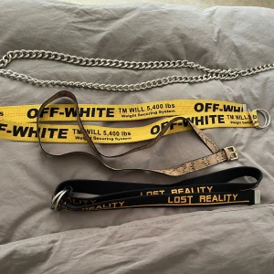 Fyra trendiga bälten, Off-White & mer - Säljer fyra bälten: ett chunky kedjebälte i silver, ett gult Off-White-bälte (INTE ÄKTA), ett smalt bälte i ormmönstrad mocka och ett svart Lost Reality-bälte med gul text. 