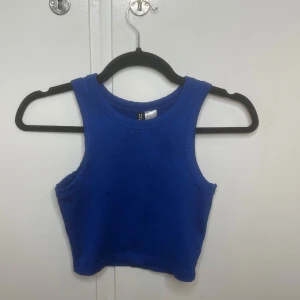 Blå ribbad linnetopp från H&M Divided - Snygg blå croppad linnetopp från H&M Divided i ribbad bomull. Modellen är ärmlös med breda axelband och rund halsringning. Perfekt för dig som gillar en enkel men trendig look. Färgen är klarblå och materialet är mjukt och stretchigt.