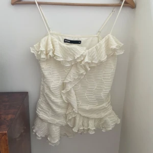 Vit omlottklänning med volanger Bik Bok - Supersöt vit kortklänning från Bik Bok med tunna axelband och omlott-design. Klänningen har volangdetaljer både upptill och nedtill, samt ett snyggt strukturerat tyg