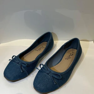 Blå jeansballerinaskor från Duffy - Snygga ballerinaskor från Duffy i blått jeanstyg med rund tå och dekorativ rosett framtill. Skorna har platt sula och är perfekta för dig som gillar en avslappnad men ändå stilren look. Passar till både jeans och klänning.