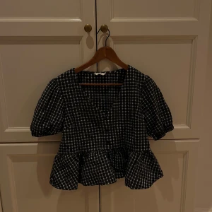 Rutig blus med volang och puffärm - Supersöt svart och vit rutig blus med v-ringning, knappar framtill och volang nertill. Säljer då den inte kommer till användning 💕💕Skriv för fler bilder 💕