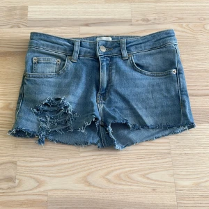 Blå jeansshorts med slitningar - Snygga blå jeansshorts med rå kant och slitningar framtill för en cool, avslappnad vibe. Klassisk femficksmodell med knapp och dragkedja. Perfekta för sommaren och har en loose passform som ger skön komfort. Varit ett bar jeans men gjort om.