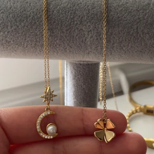 Två guldhalsband med stjärna och klöver - Säljer två snygga halsband i guldton. Ena har ett hänge med stjärna och måne dekorerad med glittriga stenar och en pärla, medan det andra har ett fyrklöverformat hänge i blank guldmetall.  Helt oanvänd och nya. Säljer antingen tillsammans eller en och en. 300 för båda eller 100kr styck. (Rostfritt)