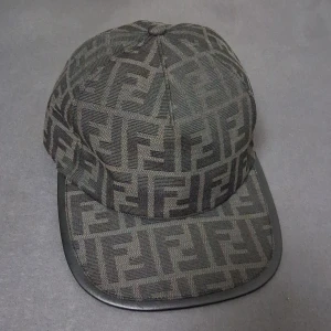 Svart Fendi keps med FF-mönster - Snygg svart keps från Fendi med ikoniskt FF-monogram över hela ytan. Kepsen har böjd skärm med läderdetalj runt kanten och justerbar rem baktill med Fendi-logga. Tillverkad i ett slitstarkt tyg som känns lyxigt och stilrent.