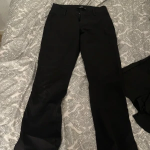 Svarta lågmidjade kostymbyxor bik bok modell Vera - Snygga svarta kostymbyxor med bootcut-snitt och klassiska hällor för bälte. Byxorna har en stilren look och passar perfekt till en dressad outfit. Materialet känns mjukt och följsamt, vilket gör dem bekväma att bära hela dagen.