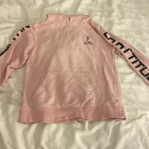 Rosa hoodie Cubus  - Säljer en ljusrosa hoodie från Cubus med svart tryck på ryggen och ärmarna. Tröjan har huva, känguruficka och coolt skateboardmotiv. Perfekt för dig som gillar streetstyle och skate. 