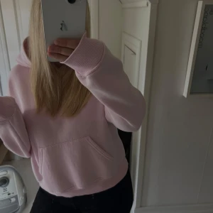 Ljusrosa hoodie med huva - Säljer en supermysig ljusrosa hoodie med stor ficka framtill och huva. Tröjan har långa ärmar med breda muddar och är perfekt för chill dagar. Passar dig som gillar en loose fit och vill ha en enkel, stilren look.