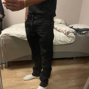 Svarta jeansbyxor från Smog - Svarta jeansbyxor från Smog med klassisk femficksdesign och raka ben. Jeansen har en mörk tvätt och subtila slitningar framtill för en avslappnad look. Tillverkade i bomullsmix som ger en skön känsla och bra passform.