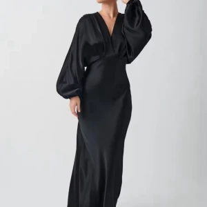 Svart satin maxi dress - Elegant svart långklänning i glansigt material med djup v-ringning och vida, långa ärmar. Klänningen har en figurnära passform över höften och faller snyggt längs kroppen. Perfekt för dig som vill sticka ut med en stilren look.