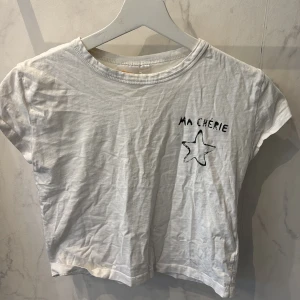 Vit t-shirt med tryck 'Ma Chérie' - Vit t-shirt i bomull med svart tryck 'Ma Chérie' och en stjärna både fram och bak. Perfekt mj till hov1 konserterna! Jag själv har använt tröjan en gång på en hov1 konsert. Modellen är croppad och har korta ärmar. Perfekt för en hov1 konsert