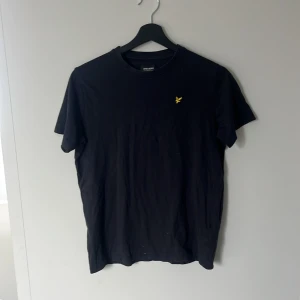 Svart t-shirt från Lyle & Scott - Svart t-shirt från Lyle & Scott med klassisk rund hals och korta ärmar. Liten gul broderad logga på bröstet ger en clean och stilren look. Storlek 12/13 men sitter som en xs