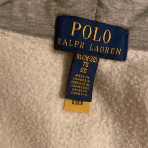 Grå hoodie från Polo Ralph Lauren XL - Säljer en grå hoodie från Polo Ralph Lauren i storlek XL. Tröjan har huva, dragkedja framtill och två fickor. Klassisk Polo-logga broderad på bröstet. Perfekt för chill dagar och enkel att matcha med jeans eller joggers.