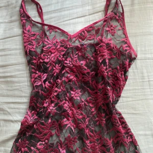 Svart och rosa spetssovklänning - Säljer en kort klänning i svart mesh med rosa broderade blommor och spetsdetaljer. Klänningen är ärmlös med tunna axelband och har en figurnära passform. Perfekt för dig som gillar statement-plagg med mycket detaljer och snygg kontrast mellan färgerna. Köpt på second hand i stockholm.
