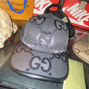 Svart keps från Gucci med GG-mönster - Snygg svart keps från Gucci med ikoniskt GG-mönster över hela kepsen. Kepsen har böjd skärm, justerbar rem bak och är tillverkad i ett mesh-liknande material som ger en cool och sportig vibe. Perfekt för dig som vill sticka ut med en lyxig accessoar.