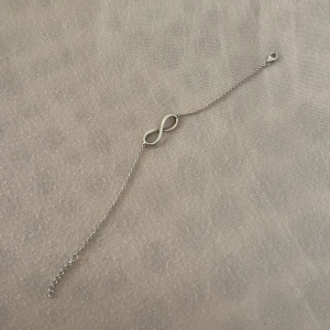 Silverfärgat armband med evighetssymbol - Snyggt och stilrent armband i silverfärg med en tunn kedja och en evighetssymbol i mitten. Armbandet är äkta silver med stämpel både på kabin haken och symbolen. Lite missfärgad men går att polera bort. Vet inte vart den är köpt men kan lösa en ask till.