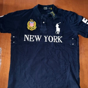 (Helt ny) Mörkblå Polo Ralph Lauren t-shirt M - Snygg mörkblå t-shirt från Polo Ralph Lauren med broderad logga och New York på bröstet. Klassisk pikékrage. detaljerade broderier. Helt ny alldig använd. Har test den en gång men den var för stor för mig. Pris kan diskuteras (k@pia)