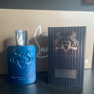 Parfums de Marly Layton 125ml - Exklusiv herrparfym, Layton Royal Essence från Parfums de Marly. Flaskan är mattblå med silverfärgad metallkork och har ett elegant reliefmönster med två hästar och sköld. Kommer i svart kartong med silverdetaljer. Volym: 125 ml.