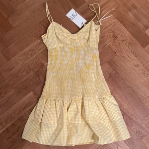Gul rutig kortklänning från Zara - Supersöt gul och vit rutig klänning från Zara med smala axelband och volangkant nertill. Den är väldigt populär och säljs inte längre! Därav pris, såklart aldrig använd då den har prislappen kvar