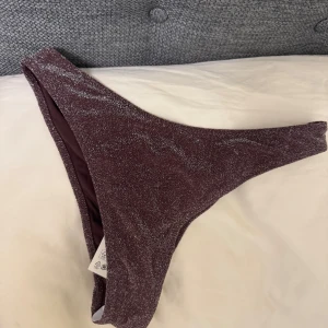 Glittrig vinröd bikiniunderdel - Supersnygg bikiniunderdel i vinröd färg med glittrigt tyg. Modellen har hög skärning och scrunch-detalj bak för en extra snygg passform. Storlek s och aldrig använt med prislapp 