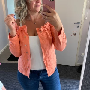 Persikofärgad omlottjacka med spänne - Säljer en persikofärgad jacka med omlottkänsla och snyggt spänne vid halsen. Jackan har långa ärmar, knappar framtill och en avslappnad passform. Perfekt för dig som vill ha en färgklick i garderoben!använd en gång.Tyvärr är förliten för mig.