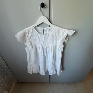 Vit blus med volang från Gina Tricot - Supersöt vit blus från Gina Tricot med volangdetaljer och korta ärmar. Blusen har knäppning bak, säljer eftersom den ej kommer till användning. Passar en xs-s men står 158/164, kan förhanhandla om priset vid snabbt köp!💕💕
