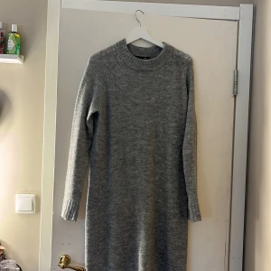 Grå stickad långklänning - Mysig grå stickad långklänning med rund hals och långa ärmar. Perfekt för kyliga dagar och enkel att styla med boots eller sneakers. Klänningen har en rak passform och ribbade detaljer vid hals och ärmslut. Storlek xs men passar mig med S!