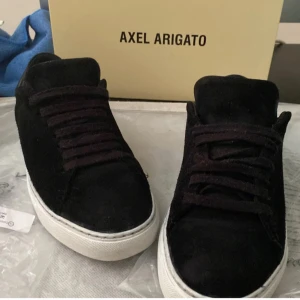Svarta sneakers från Axel Arigato - Stilrena svarta sneakers från Axel Arigato med ovandel i mocka och detaljer i skinn vid hälen. Skorna har vita, gummisulor och klassisk snörning. Perfekta för dig som gillar minimalistisk och clean design även i storlek 40. Skorna är väldigt sköna att ha på sig. Köpt för 2500kr. Kommer även med deras sko kartong och även en Axel Arigato påse. För med bilder och detaljer så får ni gärna säga till. 