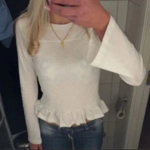 Vit smockad topp - Supersöt vit långärmad topp från Gina tricot med smockad front och volangkant nedtill. Materialet är mjukt och lätt, perfekt för dig som gillar en feminin och chill stil. Rund halsringning och lite utsvängda ärmar ger en extra touch. Storlek 146/52 men passar perfekt som xxs/xs💞