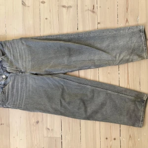 Grå jeansbyxor från H&M - Säljer ett par grå jeansbyxor från H&M i loose fit. Byxorna har en klassisk design med dragkedja och knappar framtill. Perfekta för en avslappnad stil.