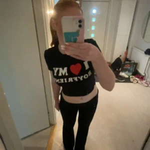 Svart croppad t-shirt med tryck - Säljer en svart croppad t-shirt med texten 'I ❤️ MY BOYFRIEND' i vitt och rött. Använd ett fåtal gånger då jag bara tagit bilder och sen tagit av mig. Säljer nu denna för jag tyvärr inte har någon användning av T-shirten.