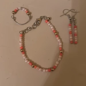 Färgglatt smyckeset - Charmigt smyckeset med armband, ring och örhängen. Alla delar har små pärlor i rosa, vitt och silver. Armbandet har en justerbar kedja, ringen är enkel och örhängena har en hängande design. Dessa är ej nickelfria och alla är hemmagjorda! 