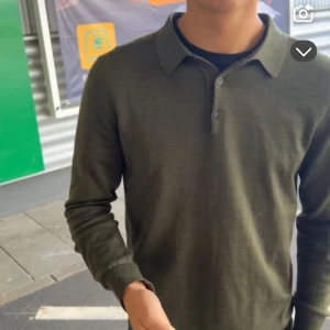 Olivgrön merinoull pikétröja - Säljer en stilren olivgrön pikétröja i mjuk merinoull. Tröjan har långa ärmar och en klassisk krage med knappar. Perfekt för en elegant och bekväm look. Passar perfekt med en skjorta undertill eller bara en vanlig vit T-shirt. (Han på bilden är 180cm)