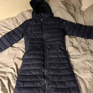 Mörkblå kappa från CRW - Säljer en mörkblå kappa från CRW. Är perfekt att rida i nu på vintern och våren då man kan ha den allt ifrån -20 till +5. Den är använd ganska mycket och de kan man se genom att den har ett hål framtill men som kan vara lätt att sy ihop, annars väldigt fint skick.