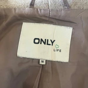 Beige kappa från ONLY - Säljer en stilren beige kappa från ONLY med ett bälte i midjan. Kappan har långa ärmar och en mjuk krage. Perfekt för höst och vår. 🧥