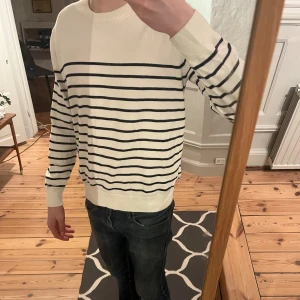 Vit och svart randig tröja från Uniqlo - Säljer en stilren vit tröja med svarta ränder från Uniqlo. Tröjan har långa ärmar och en klassisk rund halsringning. Perfekt för en avslappnad och snygg look. Skick 9/10