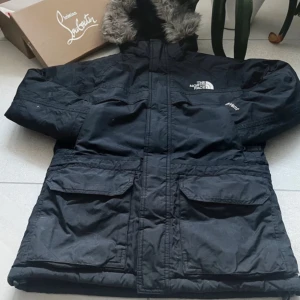 Svart vinterjacka från The North Face - Säljer en svart vinterjacka från The North Face med pälsfodrad huva. Jackan har flera praktiska fickor och stängs med dragkedja. Perfekt för kalla dagar. MVH EliteVolt
