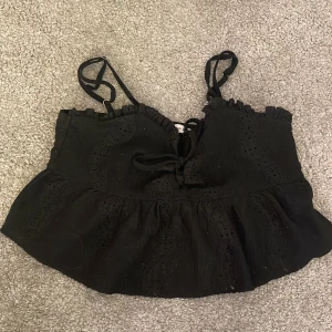 Svart croppad topp från new Yorker - Snygg svart croppad topp med axelband och knytning fram. Toppen har en volangdetalj. 