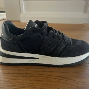 Svarta sneakers från Philippe Model - Snygga svarta sneakers från Philippe Model med en stilren design. Skorna har en kombination av skinn och mocka med en vit sula som ger en modern touch. Perfekta för en casual look. Inköpta i Philippe Model butik Milano (280 euro), knappt använda pga fel storlek, kvitto finns. 