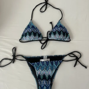 Sunny bikini Design by Si - Snygg bikini med triangelformad topp och knytband i både topp och botten. Mönstret är i blå, svart och vit med inslag av turkos och rosa. Helt ny och inte använd! Säljer för att den är tyvärr för liten för mig och jag vill inte betala returkostnader. Storlek XS!