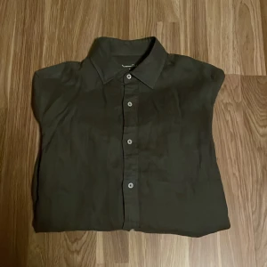Olivgrön linneskjorta från Massimo Dutti - Säljer en stilren olivgrön skjorta från Massimo Dutti i 100% linne. Skjortan har en klassisk krage och knappar framtill. Perfekt för en avslappnad men ändå elegant look. Kolla gärna in butiken, det finns möjlighet för bundle.