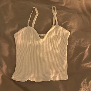 Vit ribbad linnetopp - Säljer en stilren vit ribbad linnetopp med justerbara axelband. Perfekt för varma dagar eller som ett lager under en jacka. Enkel och mångsidig design som passar till det mesta. Liten i storleken