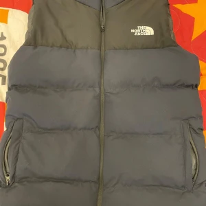 Svart,marinblå väst från The North Face - Säljer en svart,marinblå väst från The North Face med dragkedja och två fickor framtill. Perfekt för kyligare dagar och har en stilren design med logotyp på bröstet.