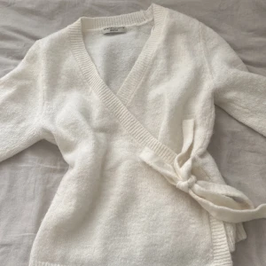 Vit omlottkofta från Gina Tricot - Säljer en stilren vit omlottkofta från Gina Tricot i premiumkvalitet. Koftan har långa ärmar och ett knytband i midjan för en justerbar passform. Perfekt för lager-på-lager under kyligare dagar. 🧣