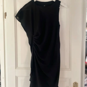 Svart klänning från H&M - Superfin svart klänning från H&M med en asymmetrisk design och draperad detalj på sidan. I mycket bra skick!🥰