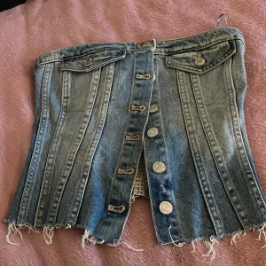 Jeans topp från Zara - Säljer en cool jeans topp  från Zara med knappar framtill och slitna detaljer. unik design med bröst  fickor och en elastisk baksida för bättre passform. Perfekt för en trendig look!