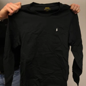 Svart långärmad tröja från Polo Ralph Lauren - Säljer en stilren svart långärmad tröja från Polo Ralph Lauren med den klassiska loggan broderad på bröstet. Perfekt för en avslappnad men ändå elegant look. Passar bra till jeans eller chinos.