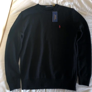 Svart stickad tröja från Ralph Lauren - Säljer en stilren svart stickad tröja från Ralph Lauren med det klassiska röda broderade logotypen på bröstet. Tröjan är helt ny och har lappen kvar. Säljer för att den var för stor för mig. Skriv vid frågor och funderingar!