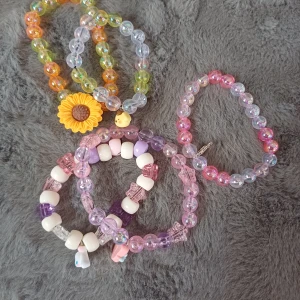 Färgglada pärlarmband - Säljer ett set med färgglada pärlarmband. Armbanden har olika färger som rosa, lila, och orange med detaljer som en solros och små berlocker. Perfekt för att lägga till en lekfull touch till din stil!