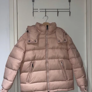 Moncler Maya Rosa  - Snygg rosa pufferjacka fràn Moncler med avtagbar huva och dragkedja. Jackan har länga ärmar och praktiska fickor med dragkedja. Perfekt för kyliga dagar. Nfc chip funkar bara inne i jackan och inte pa armen. Köptes pả auktion. Storlek XS dam storlek